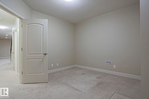 An interior room featuring neutral-toned walls, light-colored carpeting, and a white door with a silver handle - 2315 Ashcraft Cape, Edmonton, AB - Indoor Photo Showing Other Room