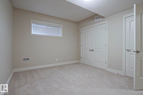 This room features neutral-toned walls, light-colored carpeting, a window with blinds, and white double doors with arch detailing - 2315 Ashcraft Cape, Edmonton, AB - Indoor Photo Showing Other Room