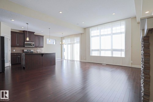 Open concept living space featuring dark hardwood floors, a kitchen with dark cabinetry and stainless steel appliances, and a large window with white blinds - 2315 Ashcraft Cape, Edmonton, AB - Indoor Photo Showing Kitchen