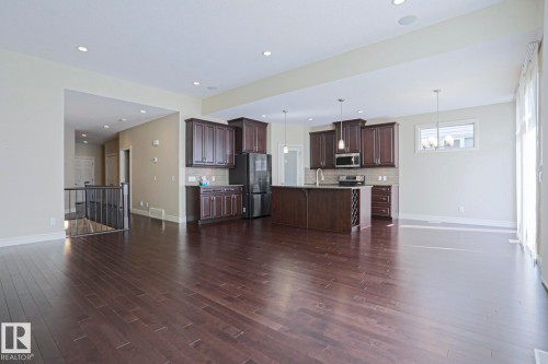The property features dark hardwood flooring throughout, a kitchen with dark cabinetry, stainless steel appliances, and an island - 2315 Ashcraft Cape, Edmonton, AB - Indoor Photo Showing Other Room