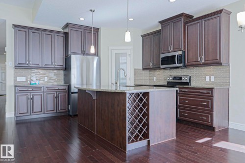 Kitchen featuring dark wood cabinetry, stainless steel appliances, a kitchen island with built-in wine storage, and pendant lighting - 2315 Ashcraft Cape, Edmonton, AB - Indoor Photo Showing Kitchen With Upgraded Kitchen