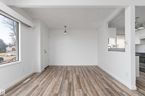 Open concept living space featuring wide plank flooring, a large window, a ceiling-mounted light fixture, and a pass-through to the kitchen - 6103-6105 97A Avenue, Edmonton, AB - Indoor Photo Showing Other Room