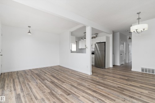Expansive living area featuring light-toned flooring, white walls, and a contemporary chandelier - 6103-6105 97A Avenue, Edmonton, AB - Indoor Photo Showing Other Room