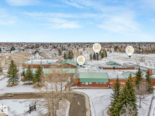 Aerial view showcasing the property's proximity to a large red brick building with a green roof, surrounded by evergreen trees and a snow-covered landscape - 4105 41 Avenue, Edmonton, AB - Outdoor With View