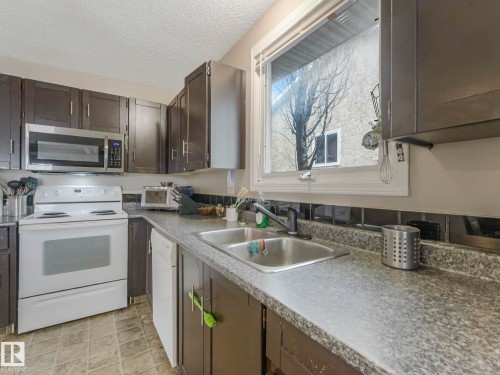 Kitchen featuring brown cabinetry, a white stove, a stainless steel microwave, a double basin sink, and a window - 4105 41 Avenue, Edmonton, AB - Indoor Photo Showing Kitchen With Double Sink