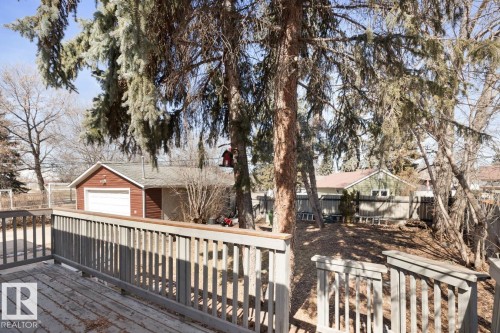 The property features a wooden deck with a railing, overlooking a yard with mature trees - 15926 92 Avenue, Edmonton, AB - Outdoor