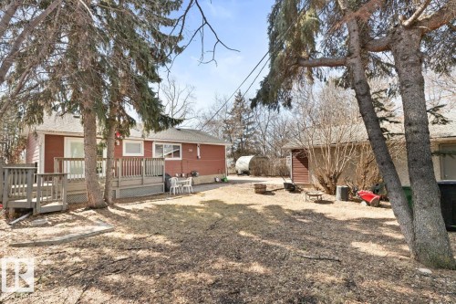 The property features a red exterior, a wooden deck, and a yard with mature trees - 15926 92 Avenue, Edmonton, AB - Outdoor