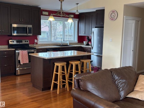 The kitchen features dark wood cabinetry, granite countertops, and stainless steel appliances, including a microwave, stove, and refrigerator - 15926 92 Avenue, Edmonton, AB - Indoor Photo Showing Kitchen