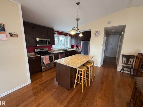 This kitchen features dark wood cabinetry, stainless steel appliances, and a central island with a light-colored speckled countertop - 15926 92 Avenue, Edmonton, AB - Indoor Photo Showing Kitchen