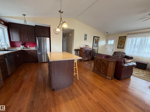 This open-concept living space features hardwood flooring throughout, a kitchen with dark wood cabinetry, stainless steel appliances, and a granite-topped island - 15926 92 Avenue, Edmonton, AB - Indoor Photo Showing Kitchen