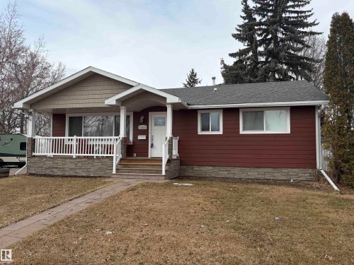 The property features a charming front porch with white railings and columns, complemented by a stone facade base - 15926 92 Avenue, Edmonton, AB - Outdoor With Deck Patio Veranda
