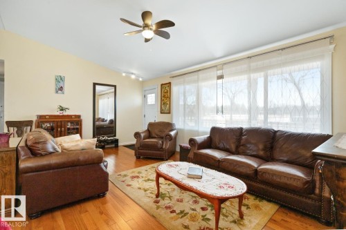 This living space features hardwood flooring, a ceiling fan with integrated lighting, and large windows with sheer coverings - 15926 92 Avenue, Edmonton, AB - Indoor Photo Showing Living Room