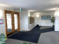 The entrance features double wooden doors with glass panels, leading into a well-lit hallway with light-colored walls - 