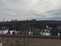 Views of a distant cityscape, surrounded by a densely treed natural area with patches of snow - 