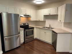 Kitchen featuring stainless steel appliances, white cabinetry, dark wood-finish flooring, light countertops, and a white tiled backsplash - 