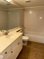 Bathroom featuring a white vanity with paneling and brushed nickel hardware, an integrated oval sink, a large wall-mounted mirror, a standard toilet, and a bathtub with white subway tile surround and brass fixtures - 