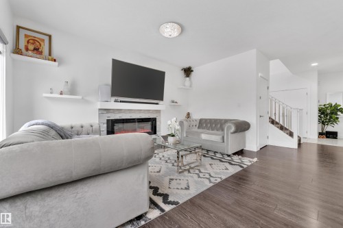The living area features dark wood-style flooring, a fireplace with a stone-look surround, and a staircase with white railings - 2630 16A Ave Nw, Edmonton, AB - Indoor Photo Showing Living Room With Fireplace
