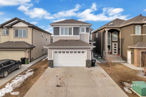 The property features a two-story design with light-toned siding and dark grey accents, a two-car garage, and a concrete driveway - 2630 16A Ave Nw, Edmonton, AB - Outdoor