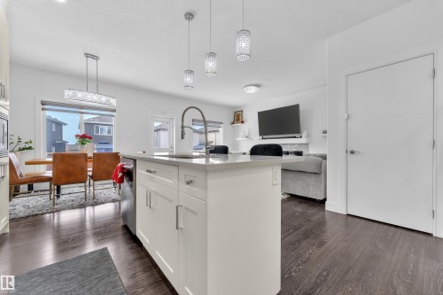 This open-concept living space features hardwood floors, a kitchen island with a sink and pendant lighting, and a dining area with a large window - 2630 16A Ave Nw, Edmonton, AB - Indoor Photo Showing Kitchen