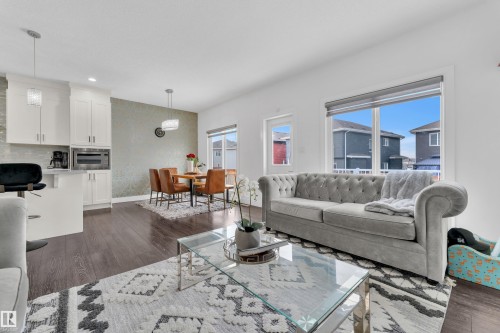 The property features an open living area with dark hardwood floors, large windows providing natural light, and a kitchen island with white cabinetry - 2630 16A Ave Nw, Edmonton, AB - Indoor Photo Showing Living Room