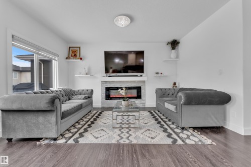 Living area featuring a modern electric fireplace with a stacked stone facade and a white mantel, complemented by dark wood flooring and light walls - 2630 16A Ave Nw, Edmonton, AB - Indoor Photo Showing Living Room With Fireplace
