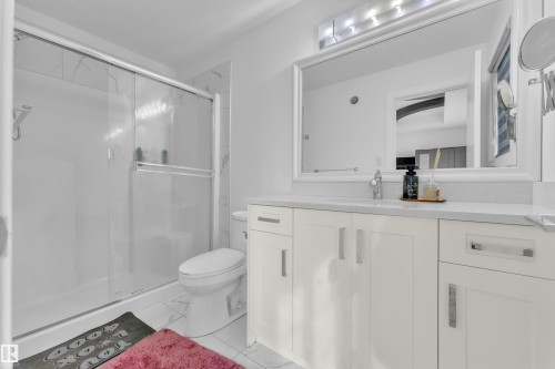 Bathroom featuring a glass-enclosed shower, a toilet, a vanity with a white countertop, and a mirror above the vanity - 2630 16A Ave Nw, Edmonton, AB - Indoor Photo Showing Bathroom