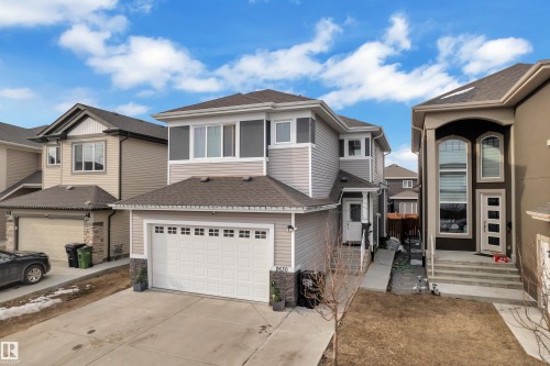 The property features an attached garage with a concrete driveway, light-colored siding, and a partial stone facade - 2630 16A Ave Nw, Edmonton, AB - Outdoor