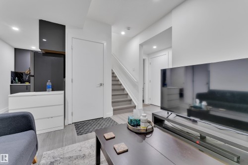 Living area featuring light-colored flooring, white walls, and a staircase with white railings - 2630 16A Ave Nw, Edmonton, AB - Indoor