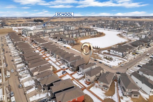 Aerial view showcasing the property's location within a developed neighborhood, featuring residential homes, a nearby body of water, and a school in the distance - 2630 16A Ave Nw, Edmonton, AB - Outdoor With View