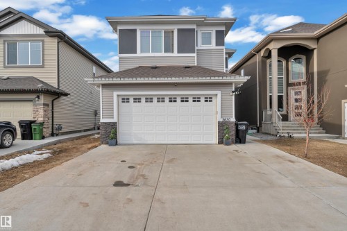 The property features a two-story exterior with light gray siding and dark gray accents, a prominent two-car garage with a concrete driveway, and a stone accent column near the garage entrance - 2630 16A Ave Nw, Edmonton, AB - Outdoor