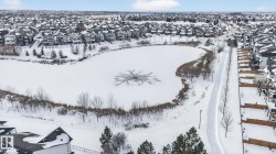 Aerial view showcasing the surrounding neighborhood, featuring a snow-covered pond with visible ice formations, and a paved pathway running alongside the pond - 