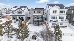 The property features a modern exterior with a dark roof and light siding, a ground-level patio, and an upper-level balcony with a glass railing - 