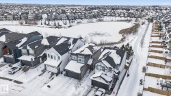 Aerial view of the property and surrounding neighborhood, featuring a frozen pond and snow-covered streets - 