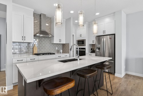 The kitchen features white cabinetry, stainless steel appliances, a grey subway tile backsplash, and an island with a light-colored countertop - 3230 Parker Loop, Edmonton, AB - Indoor Photo Showing Kitchen With Double Sink With Upgraded Kitchen