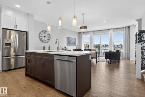 Open concept living area with hardwood floors, a kitchen island featuring a sink and dishwasher, white cabinetry, and stainless steel appliances - 3230 Parker Loop, Edmonton, AB - Indoor Photo Showing Kitchen With Upgraded Kitchen