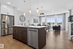 Open concept living area with hardwood floors, a kitchen island featuring a sink and dishwasher, white cabinetry, and stainless steel appliances - 