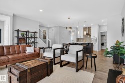 The property features an open concept living area with light-toned flooring, a staircase with white risers and dark handrails, and a kitchen with white upper cabinetry and dark lower cabinetry - 