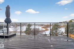 The property features an outdoor deck with glass railings, offering views of a snow-covered landscape, bare trees, and distant houses under a clear sky - 