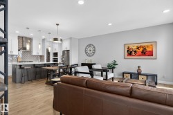 This open-concept living area features light wood flooring, recessed lighting, and a kitchen with white cabinetry, a large island, stainless steel appliances, and pendant lighting - 