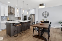 The kitchen features white cabinetry, a gray subway tile backsplash, and a large island with a white countertop - 
