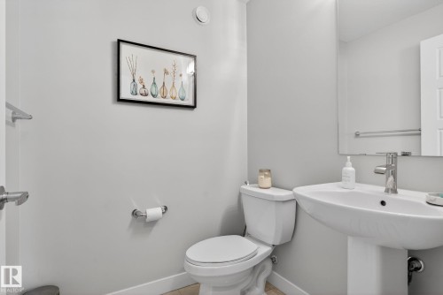 Bathroom featuring a white pedestal sink with a chrome faucet, a white toilet, and a wall-mounted mirror - 3230 Parker Loop, Edmonton, AB - Indoor Photo Showing Bathroom