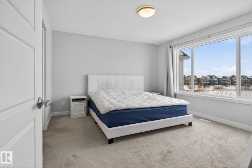 The property features a bright room with carpeted flooring, a large window providing views of the surrounding neighborhood, and neutral wall paint - 3230 Parker Loop, Edmonton, AB - Indoor Photo Showing Bedroom