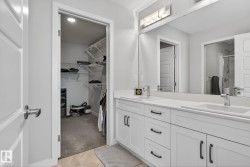 Bathroom featuring a dual vanity with white cabinetry and chrome fixtures, illuminated by a light bar above the mirror - 