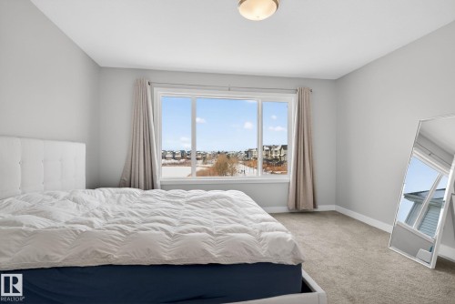 This room features light grey walls and carpet, with a large window providing ample natural light and views of the surrounding neighborhood - 3230 Parker Loop, Edmonton, AB - Indoor Photo Showing Bedroom
