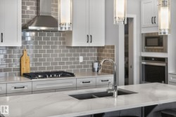The kitchen features white cabinetry, a gas cooktop, stainless steel appliances, and a central island with an undermount sink and a gooseneck faucet - 