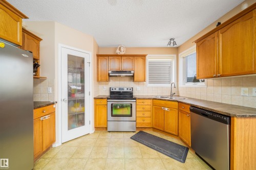 The kitchen features wood cabinetry, stainless steel appliances, and tiled flooring - 8932 175 Avenue, Edmonton, AB - Indoor Photo Showing Kitchen With Double Sink