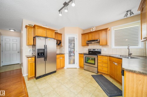 The kitchen features light wood cabinetry, stainless steel appliances, a double basin sink, and tile flooring - 8932 175 Avenue, Edmonton, AB - Indoor Photo Showing Kitchen With Double Sink