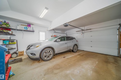 The property includes a garage with a white sectional overhead door and concrete flooring, featuring overhead lighting and wall-mounted shelving - 8932 175 Avenue, Edmonton, AB - Indoor Photo Showing Garage