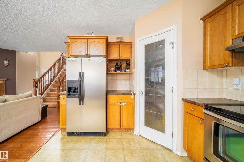 The kitchen features wood cabinetry, a stainless steel side-by-side refrigerator, a stainless steel oven with a stovetop, and tiled flooring - 8932 175 Avenue, Edmonton, AB - Indoor Photo Showing Kitchen