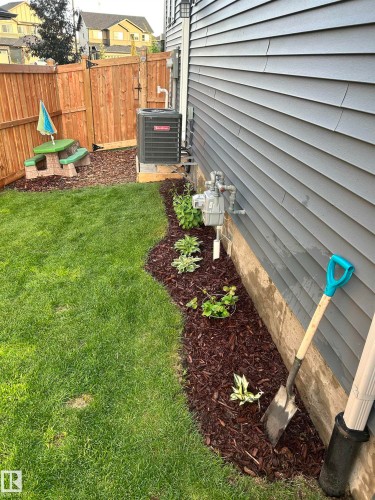 This property features a neatly maintained lawn and a landscaped bed with dark wood chip mulch and green plantings - 7490 Creighton Place, Edmonton, AB - Outdoor